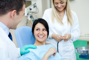 A woman is seated in a dental chair, with dentists beside her