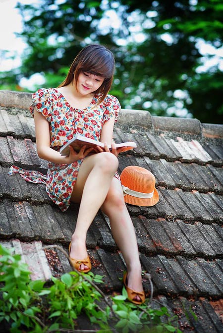 A woman relaxes on a rooftop, deeply focused on reading a book