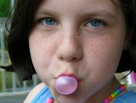 A young girl blowing a bubble with her gum