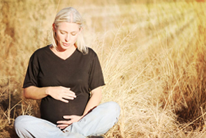 A pregnant women is sting in the hay field